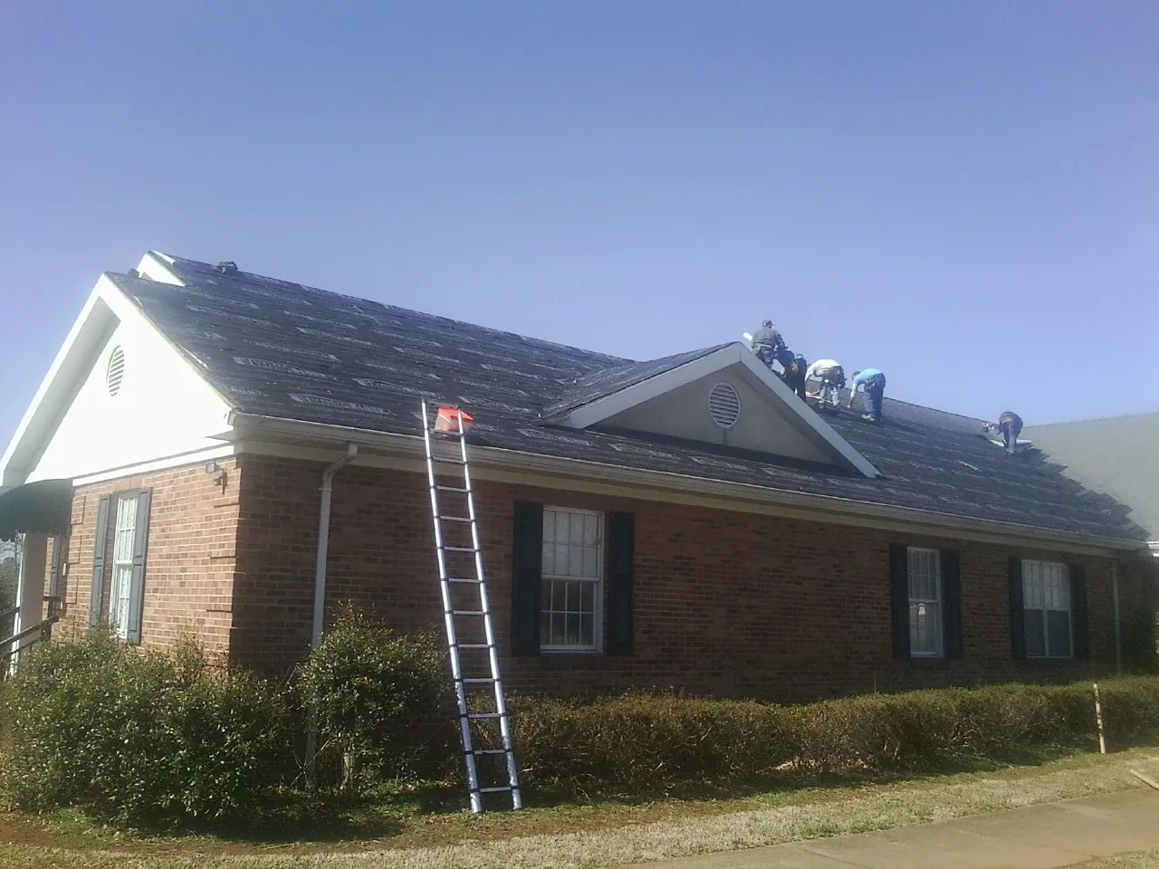 Crew tearing shingles off a brick ranch roof with a ladder set — Metal Roof Repair work by our crew in Gypsum