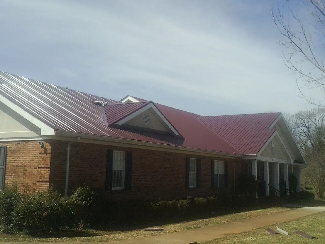 Red metal roof with gabled entries on a long brick building, from a Hail Damage Roof Repair job in Gypsum